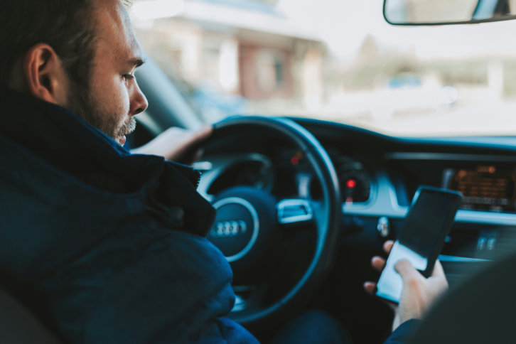 Foto eines Autofahrers mit Handy in der Hand